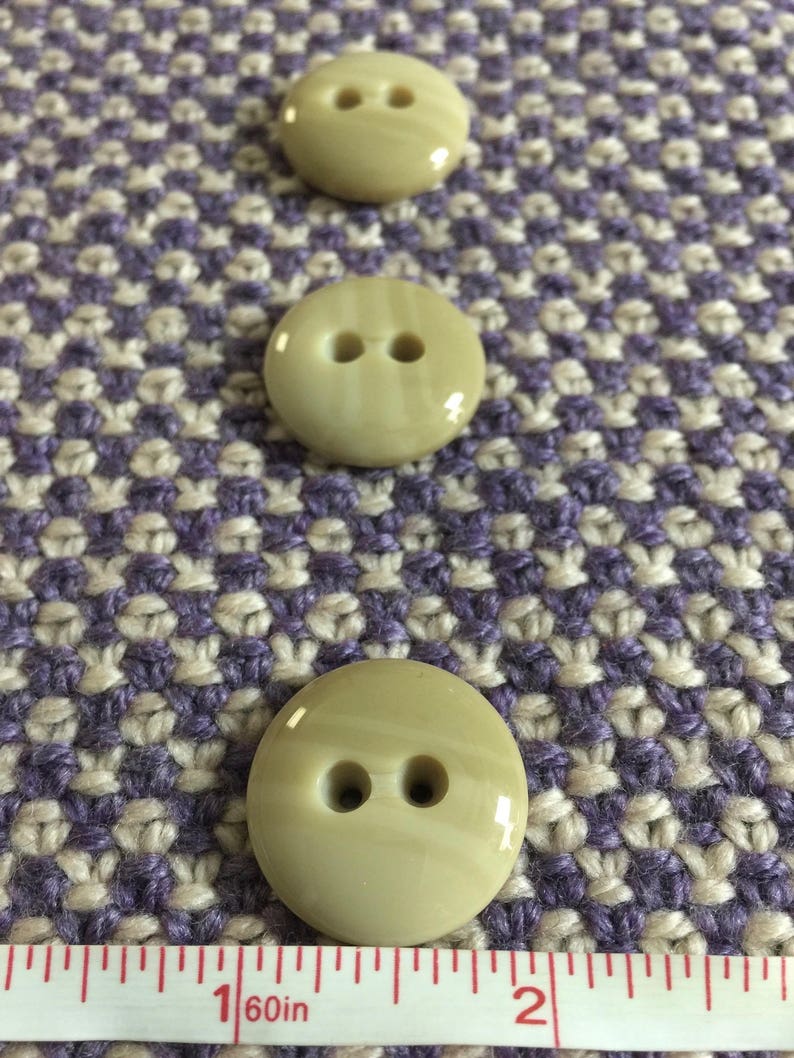 May include: Three beige plastic buttons with two holes each. The buttons are approximately 1 inch in diameter.