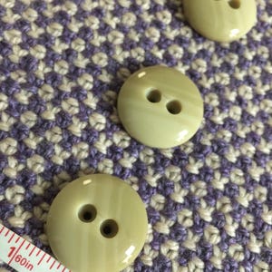 May include: Three light green plastic buttons with two holes each. The buttons have a striped pattern and a glossy finish.