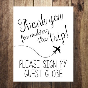 May include: White sign with black text that says "Thank you for making the trip!" with a small airplane icon below the text. Below the airplane is more black text that says "Please sign my guest globe."