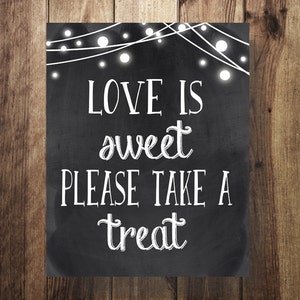 Può includere: Un cartello nero in ardesia con testo bianco che recita "L'amore è dolce, prendi un dolcetto". Il cartello è decorato con luci a stringa bianche.