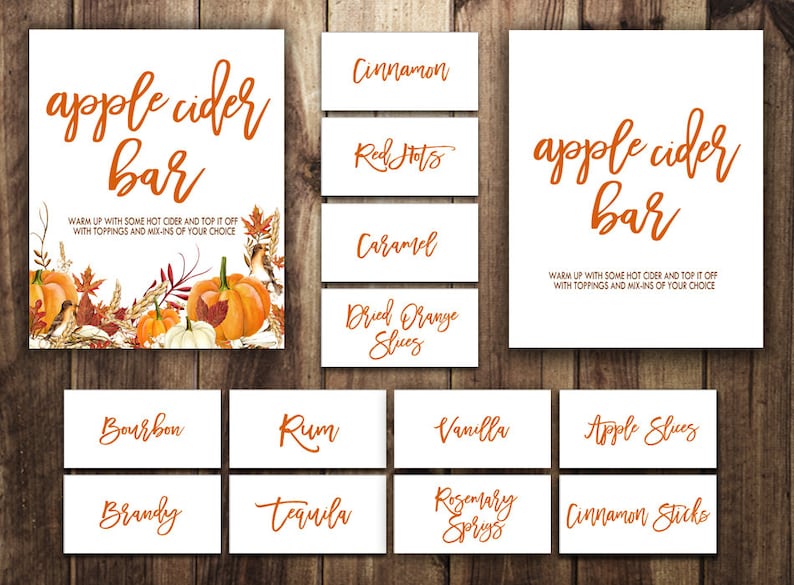 May include: Printable signs for an apple cider bar with fall-themed decorations. The signs include "apple cider bar", "cinnamon", "red hots", "caramel", "dried orange slices", "bourbon", "rum", "vanilla", "apple slices", "brandy", "tequila", "rosemary sprigs", and "cinnamon sticks".