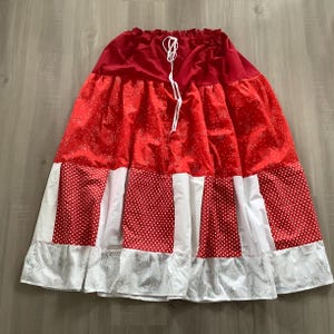 May include: A red and white tiered skirt with a white drawstring waist. The skirt has a red floral print on the top tier, white polka dots on the middle tier, and a white floral print on the bottom tier.