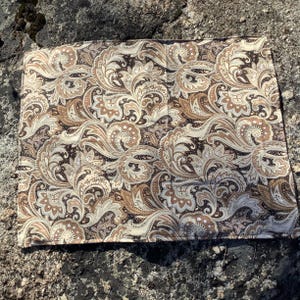 May include: A square fabric handkerchief featuring a detailed paisley pattern in shades of dark brown, tan, and cream. The intricate design consists of swirling teardrop shapes, floral motifs, and small dots covering the entire surface area.