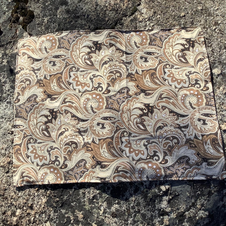 May include: A square fabric handkerchief featuring a detailed paisley pattern in shades of dark brown, tan, and cream. The intricate design consists of swirling teardrop shapes, floral motifs, and small dots covering the entire surface area.