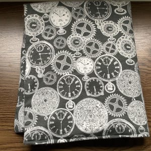 May include: A folded piece of dark grey fabric featuring a repeating white print of various vintage pocket watches, clock faces with Roman and Arabic numerals, and intricate mechanical gear patterns arranged in a dense, overlapping composition.
