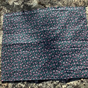 May include: A rectangular fabric piece featuring a dark forest green background with a dense, repeating pattern of small pink rose blossoms and tiny white dots. The textile has a finished hem along the top edge and a flat, smooth surface texture.