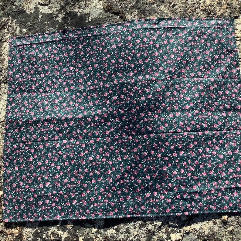 May include: A rectangular fabric piece featuring a dark forest green background with a dense, repeating pattern of small pink rose blossoms and tiny white dots. The textile has a finished hem along the top edge and a flat, smooth surface texture.