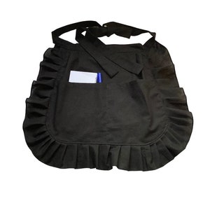 May include: A black ruffled apron with a pocket and a white card holder. The apron has a simple design and is perfect for a variety of tasks.