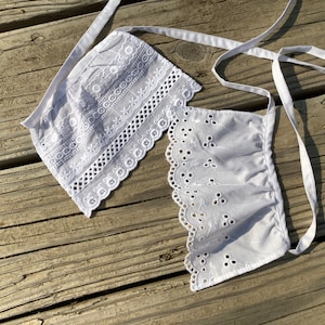 May include: White cotton lace trim with a delicate floral pattern. The trim is made of a soft, lightweight fabric and has a scalloped edge.