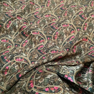 May include: Close-up of a fabric with a paisley pattern. The fabric features a dark brown background with intricate designs in shades of green, tan, and pink. The paisley shapes are outlined in a lighter tan color.