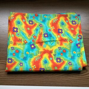 May include: A square fabric piece featuring a vibrant tie-dye background in shades of orange, yellow, and turquoise. The pattern is decorated with small, repeating illustrations of purple, red, and yellow flowers along with green leaf shapes.