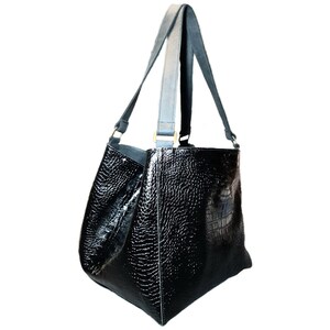 May include: A black leather tote bag with a crocodile embossed pattern and two long straps. The bag has a boxy shape and gold hardware.