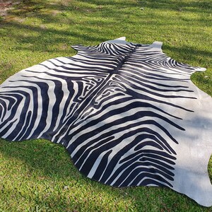 May include: A black and white zebra print cowhide rug. The rug is laid out on a green grassy lawn.