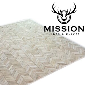 May include: A white cowhide rug with a herringbone pattern. The rug is made of natural leather and has a rustic, farmhouse style. Mission Hides & Knives is printed on the rug.