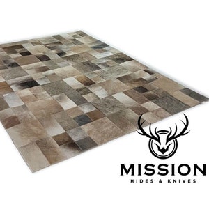 May include: A patchwork cowhide rug featuring a light brown, grey, and white colour scheme. The rug is crafted from individual pieces of leather stitched together to create a distinctive and stylish design. The rug is made by Mission Hides & Knives.