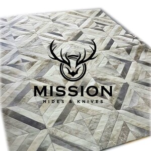 Puede incluir: Una alfombra de patrón geométrico hecha de piel de vaca en tonos grises y blancos. La alfombra presenta un logotipo para Mission Hides & Knives.