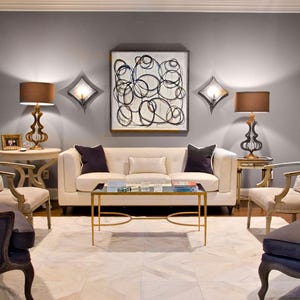 Puede incluir: Una sala de estar con un sofá gris, dos sillones, una mesa de café y dos lámparas. Las paredes están pintadas de gris y el suelo está cubierto con una alfombra blanca. Hay una pintura abstracta en blanco y negro colgada en la pared.