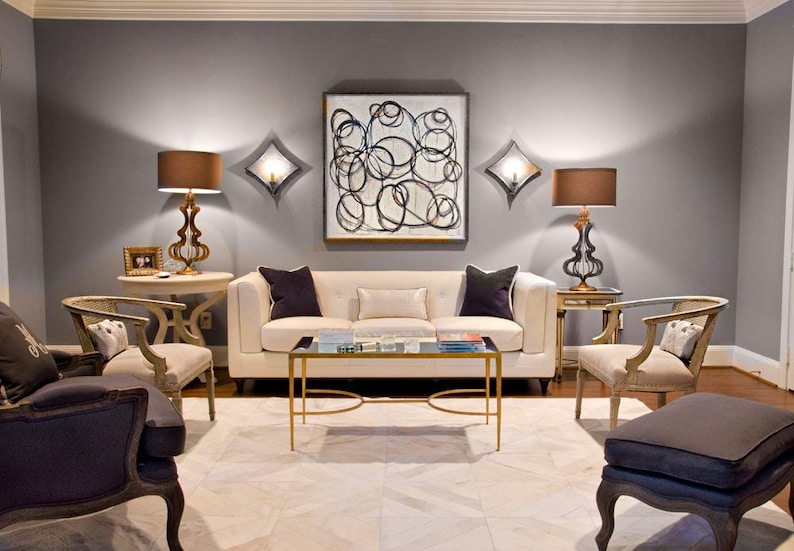 May include: A living room with a gray sofa, two armchairs, a coffee table, and two lamps. The walls are painted gray, and the floor is covered in a white rug. There is a black and white abstract painting hanging on the wall.