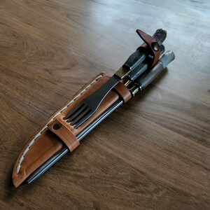 Puede incluir: Una funda de cuero marr&oacute;n con costuras blancas contiene un juego de tres pinchos de metal y un tenedor. Los pinchos y el tenedor son todos negros.