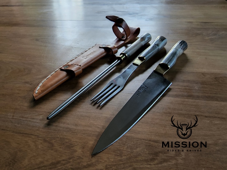 Puede incluir: Un juego de tres cuchillos de cocina con mangos de madera. Los cuchillos est&aacute;n sobre una superficie de madera. El juego incluye un cuchillo para trinchar, un tenedor y un cuchillo de chef. El cuchillo de chef tiene una hoja negra y las palabras "Mission Hides & Knives" est&aacute;n impresas en la superficie.