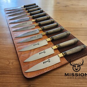 May include: A brown leather knife roll with 12 slots for knives. The roll is open and the knives are visible. The knives have wooden handles and are made by Mission Hides & Knives.