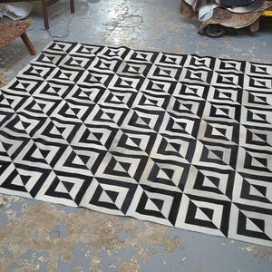 May include: Black and white geometric patterned rug with a 3D effect. The rug is made of cowhide and has a unique design.