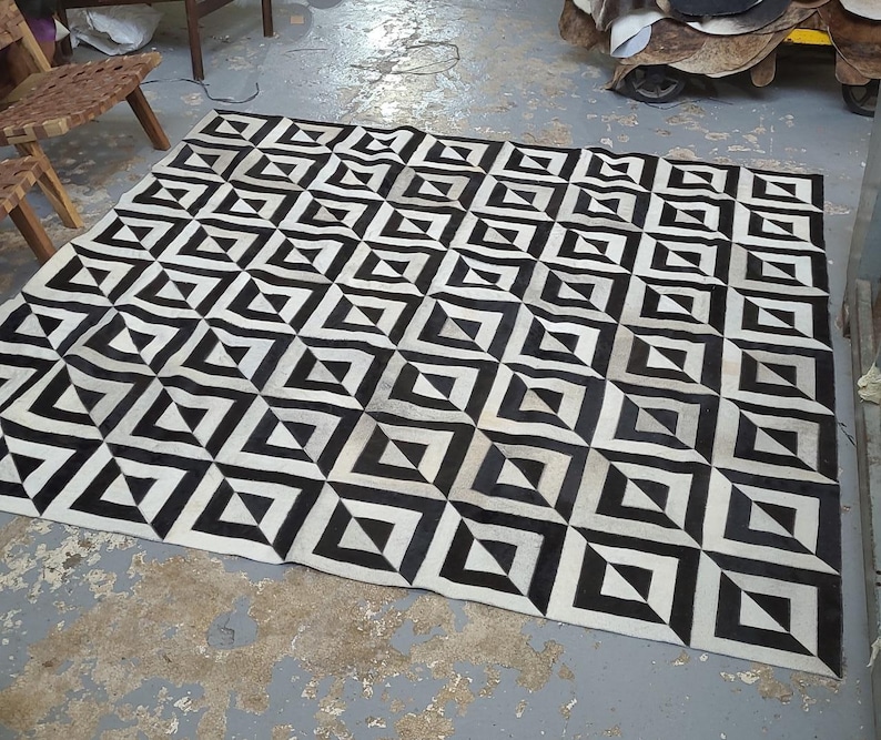 May include: Black and white geometric patterned rug with a 3D effect. The rug is made of cowhide and has a unique design.