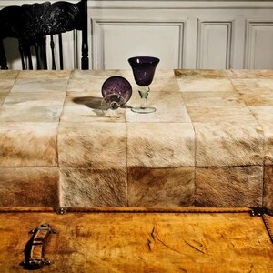 May include: A brown leather table cloth with a patchwork design. Two clear glass wine glasses with purple stems are on the table. A wooden chest with a brass latch is in the foreground.