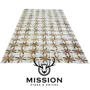 May include: A white leather rug with a geometric pattern of brown and gray circles and ovals. The rug is made of cowhide and has a unique, handcrafted look. Mission Hides & Knives is printed at the bottom of the image.