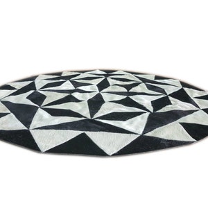 Puede incluir: Una alfombra redonda de piel de vaca negra y blanca con un patrón geométrico. La alfombra está hecha de cuero y tiene una textura suave y lujosa.