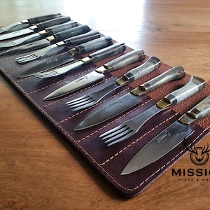 May include: A set of 10 knives and forks with brown leather handles and brass accents are displayed in a brown leather roll. The roll has the text "MISSION HIDES & KNIVES" printed on it.