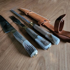 Puede incluir: Un juego de tres cuchillos de cocina con mangos de asta de ciervo y una funda de cuero. Los cuchillos incluyen un cuchillo para trinchar, un tenedor y un afilador.