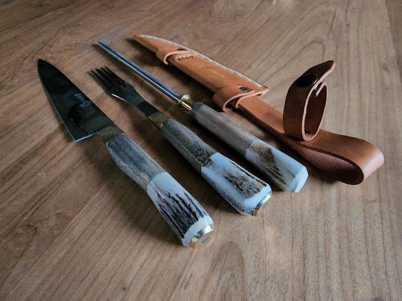 Puede incluir: Un juego de tres cuchillos de cocina con mangos de asta de ciervo y una funda de cuero. Los cuchillos incluyen un cuchillo para trinchar, un tenedor y un afilador.
