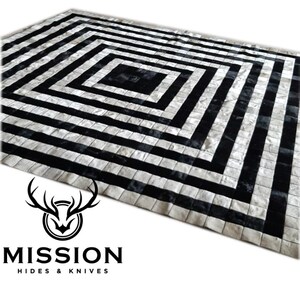 May include: Black and white cowhide rug with a geometric pattern. The rug is made of squares and rectangles, and the pattern is a series of concentric squares.