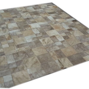 Puede incluir: Una alfombra de patchwork hecha de varias piezas de cuero marrón y beige. La alfombra está compuesta por cuadrados y rectángulos de diferentes tamaños.