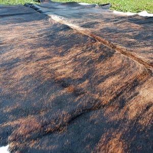 May include: A brown and black cowhide rug with a natural, mottled pattern. The rug is made of real cowhide and has a soft, luxurious feel.