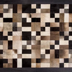 May include: A black and white patchwork rug made of cowhide. The rug is made up of squares of different sizes and colours. The rug is perfect for adding a touch of rustic charm to any room.