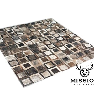 May include: A brown and grey patchwork rug made of leather squares. The rug has a geometric pattern and is made of different shades of brown and grey leather.