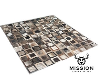May include: A brown and gray patchwork rug made of leather squares. The rug has a geometric pattern and is made of different shades of brown and gray leather.