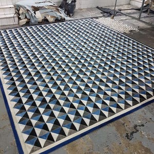 May include: A geometric patterned rug with a blue, white, and black design. The rug has a blue border and is made of leather.