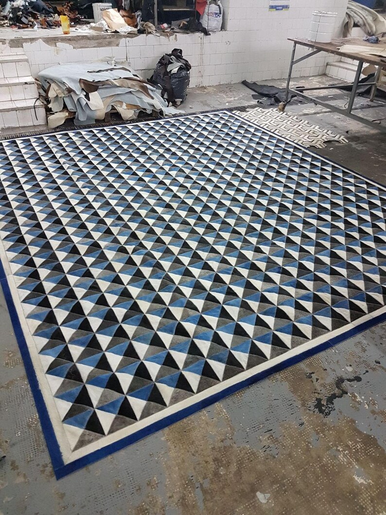 May include: A geometric patterned rug with a blue, white, and black design. The rug has a blue border and is made of leather.