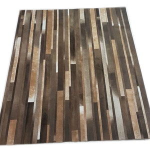 May include: A brown and white striped cowhide rug with a modern design. The rug is made of strips of leather sewn together to create a geometric pattern.