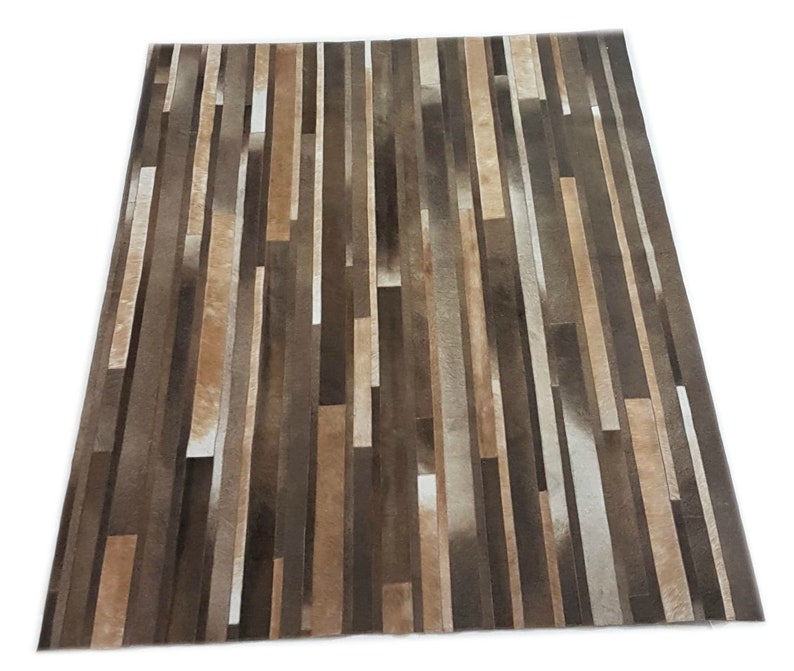 May include: A brown and white striped cowhide rug with a modern design. The rug is made of strips of leather sewn together to create a geometric pattern.