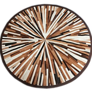 May include: Round brown, black, and white leather rug with a geometric pattern. The rug is made of strips of leather that are arranged in a radial pattern.