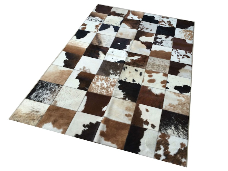 Op de afbeelding: Een rechthoekig patchwork kleed met een dambordpatroon. Het kleed is samengesteld uit vierkanten van koeienhuid in bruin, wit en zwart. Het patroon van het kleed cre&euml;ert een textuurrijk oppervlak, geschikt voor interieurdecoratie.