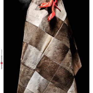 May include: A patchwork rug made of different shades of brown and white cowhide. A pair of red high-heeled shoes are placed on top of the rug.