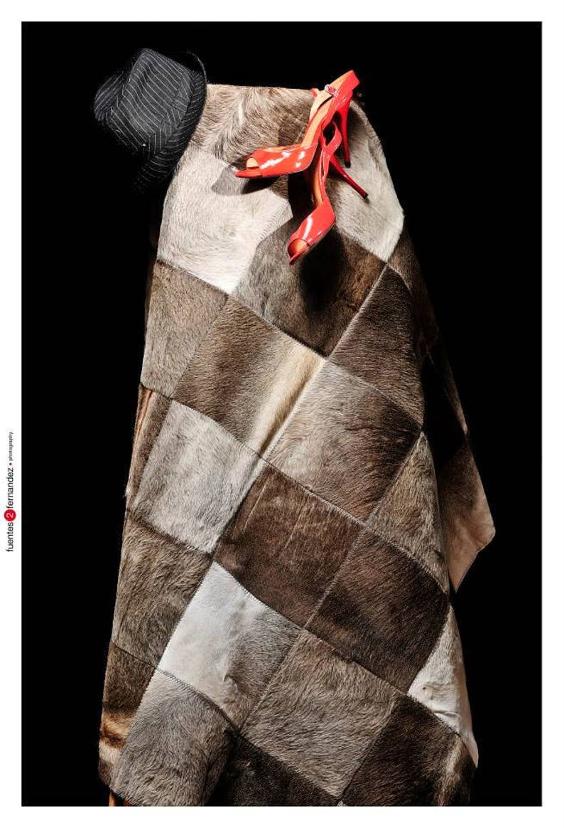 May include: A patchwork rug made of different shades of brown and white cowhide. A pair of red high-heeled shoes are placed on top of the rug.