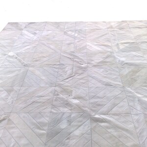 May include: White leather rug with a geometric pattern. The rug is made of cowhide and has a natural, rustic look.