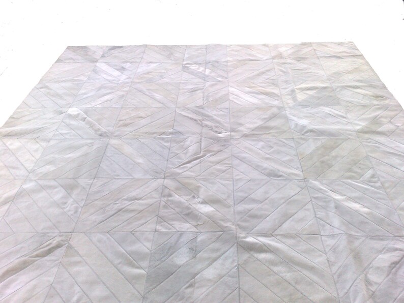 May include: White leather rug with a geometric pattern. The rug is made of cowhide and has a natural, rustic look.