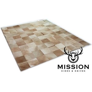 Puede incluir: Una alfombra de piel de vaca de color marrón claro hecha de cuadrados de cuero. La alfombra está hecha de diferentes tonos de cuero marrón claro. La alfombra está sobre un fondo blanco.